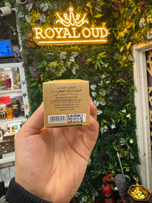 Hand holding Arabian perfume box in front of floral shop display and illuminated signage