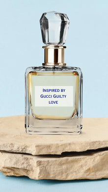 Clear glass perfume bottle with crystal cap, labeled 'Inspired by Gucci Guilty Love', on stone slab