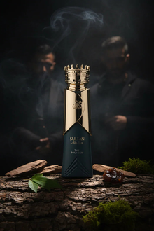 Luxurious Sultan oud perfume bottle with gold crown cap, surrounded by wood, resin, and green leaves, set against a smoky dark background.