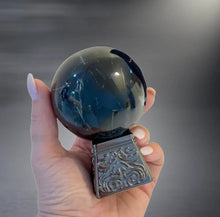 Hand holding black crystal ball with ornate silver base, glossy surface, neutral background