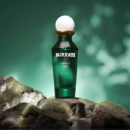 Surrati Fabrica 1929 perfume bottle with green glass and white cap on stone, green background