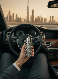 Luxury silver Arabian oud perfume bottle held in car with city skyline view