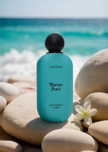 Blue Marine Pearl perfume bottle by Naseem on beach rocks with ocean waves and a white flower