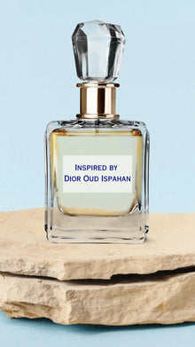 Glass perfume bottle with crystal cap and gold accent, labeled Inspired by Dior Oud Ispahan, on stone slab