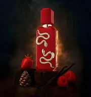 Red perfume bottle with gold accents on a dark background with berries and a pine cone.