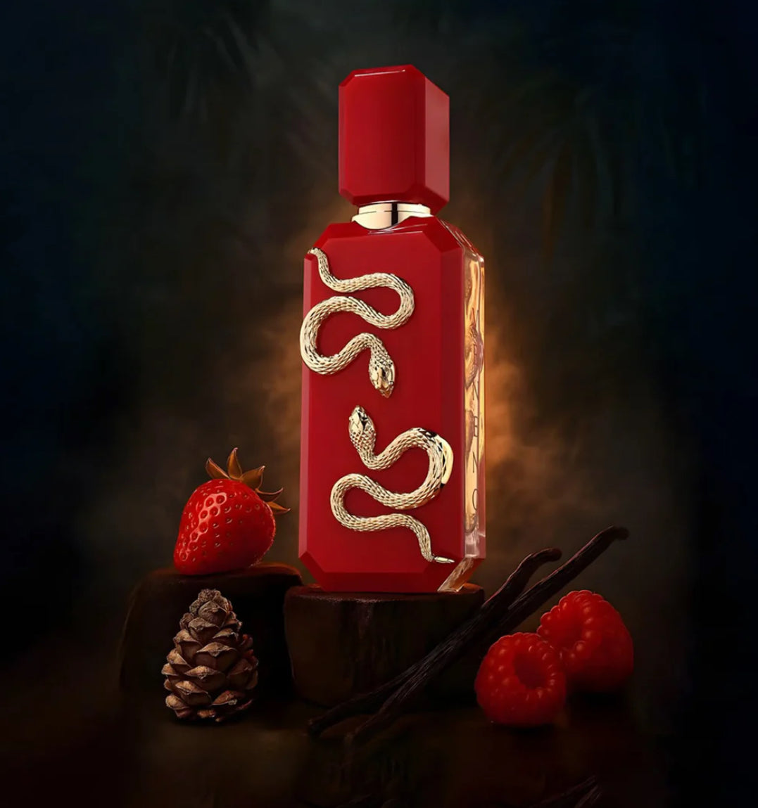 Red perfume bottle with gold accents on a dark background with berries and a pine cone.