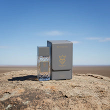 Bujarami oud perfume bottle and box on a rock outdoors under a clear blue sky.