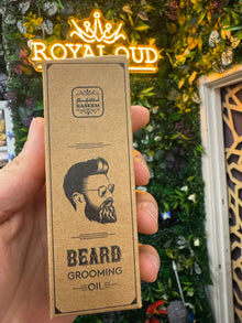 Hand holding Naseem beard grooming oil box with illustrated bearded man, leafy shop background