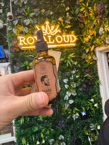 Hand holding beard grooming oil bottle in front of lush green wall and neon sign