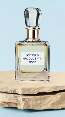 Elegant glass perfume bottle with crystal cap labeled inspired by oud satin mood, on stone slab.