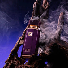 Cocoa Morado oud perfume bottle in deep purple with gold accents, surrounded by wood and smoke.