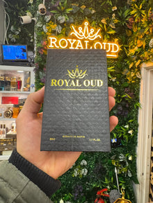 Hand holding Royal Oud perfume box in front of floral store display