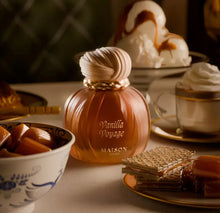 Vanilla Voyage perfume bottle with caramel candies, wafers, and desserts on elegant table setting