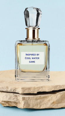 Clear glass Arabian oud perfume bottle with gold accent, label reads 'Inspired by Cool Water Game', on stone slab