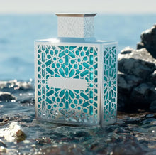 Elegant Arabian oud perfume bottle with geometric design near ocean rocks