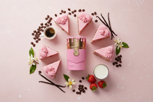 Pink oud perfume bottle with gold cap surrounded by strawberry cake slices, coffee, and vanilla pods on a pastel pink background