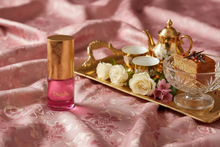 Arabian oud perfume bottle with gold cap, flowers, tea set, and cake on pink fabric