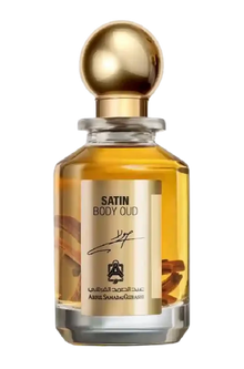 Clear glass bottle of Satin Body Oud perfume with gold cap and visible oud wood pieces inside.