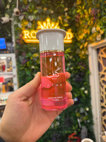 Hand holding Kaaf Pink extrait de parfum bottle, 100ml, with lush floral background.