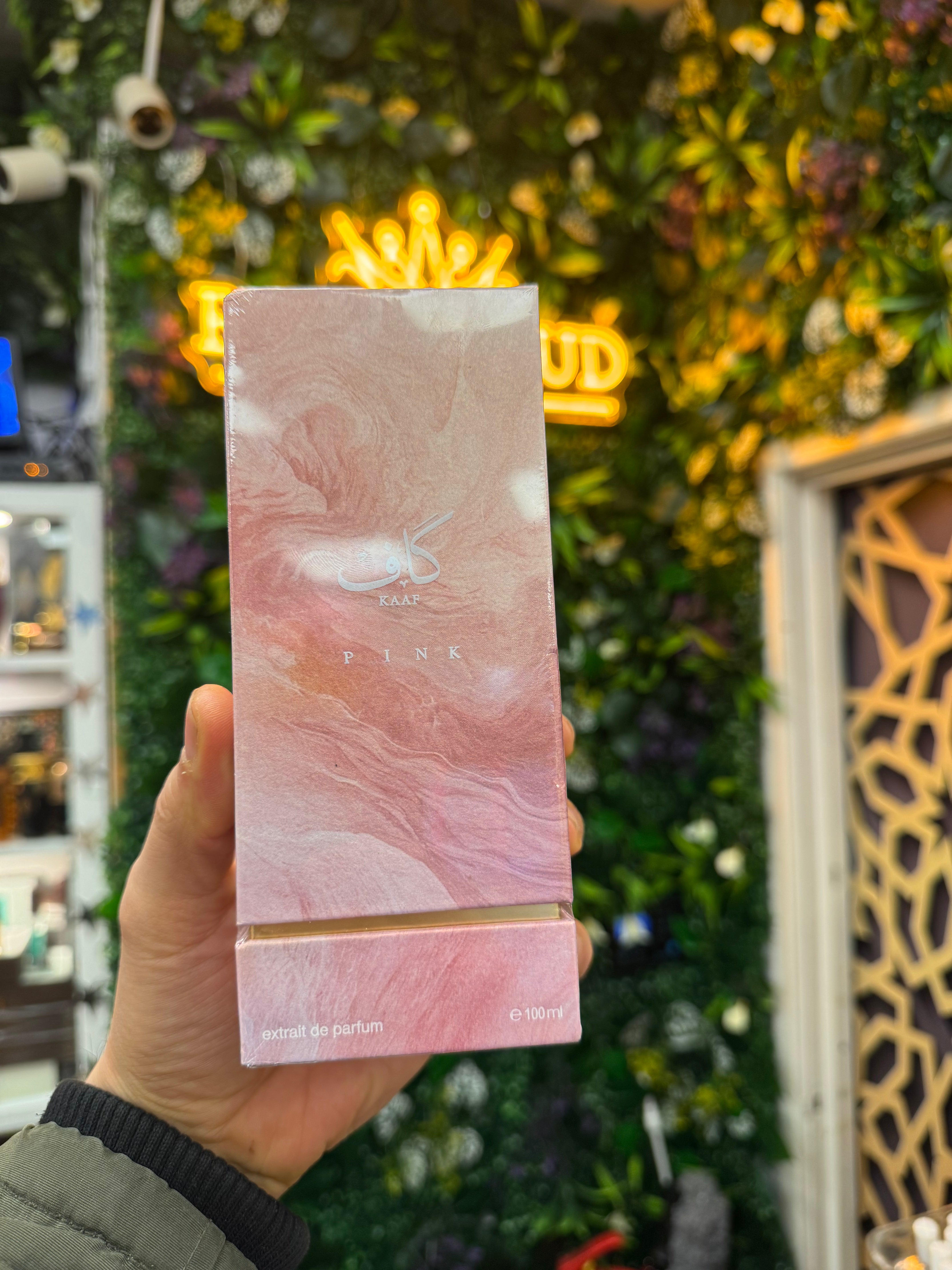 Pink perfume box held in front of a decorative wall with neon lights
