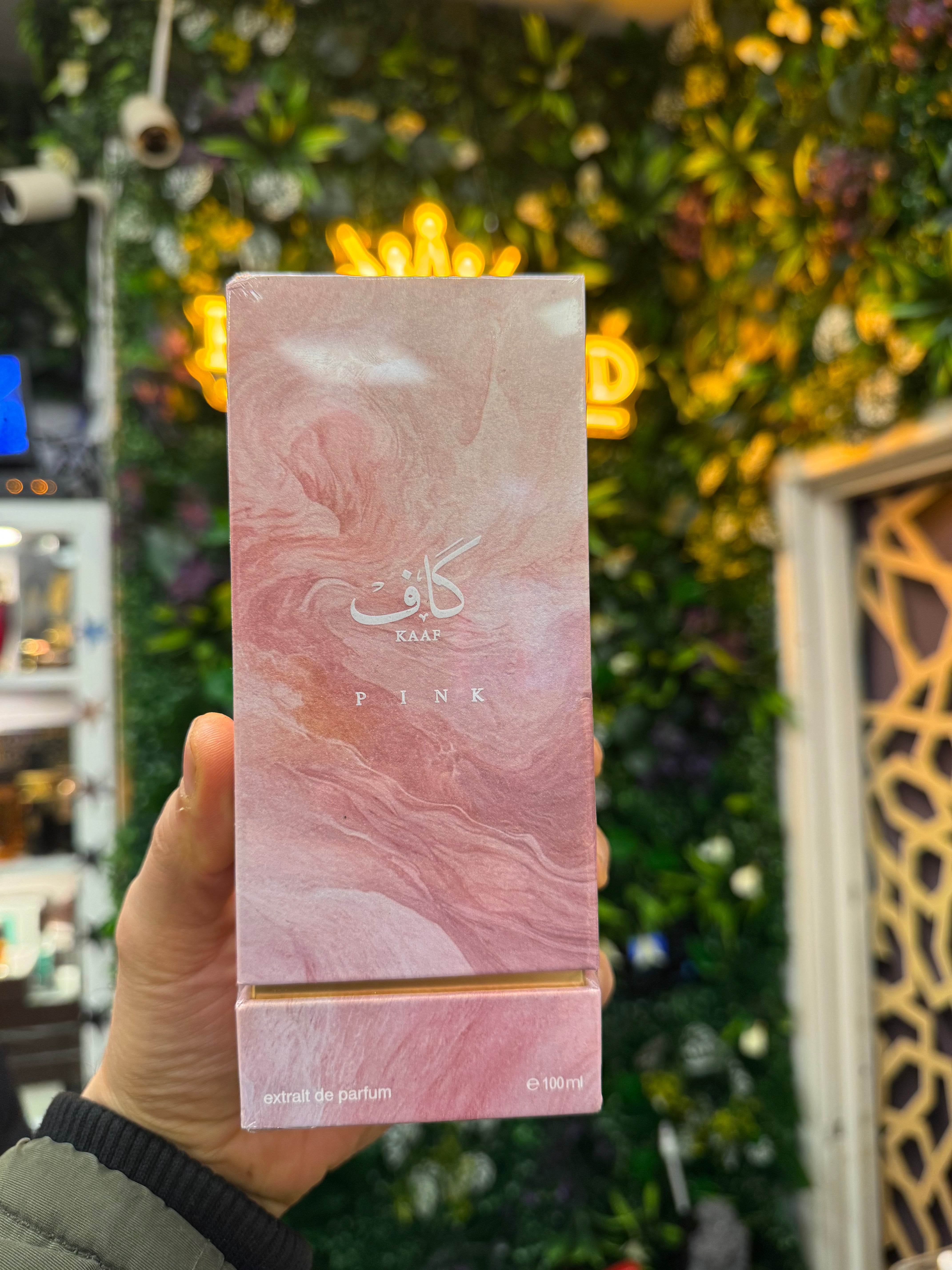 Pink perfume bottle with 'PINK' branding held in front of a decorative background.