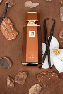 Liquid Brun perfume bottle with orchid flower, vanilla pods, and wood pieces on brown background