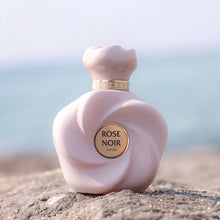 Rose Noir perfume bottle with rose-inspired design placed on rocks by the sea