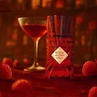 Arabian oud perfume bottle with red berries and a cocktail glass on a rich red background