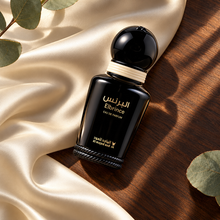 Overhead Elbrince EDP 15ml bottle on ivory satin and dark wood with eucalyptus leaves