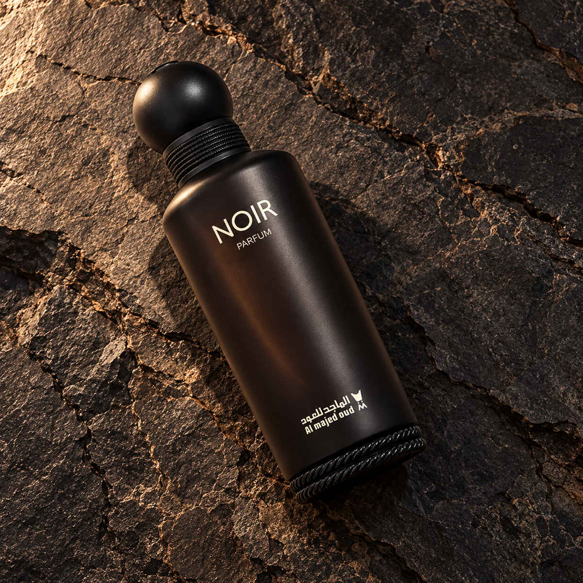 Overhead photograph of Al Majed Oud Noir Parfum bottle lying diagonally on textured stone