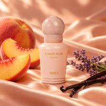 Candy Musk perfume oil bottle on peach satin beside peach slices, lavender and vanilla pods