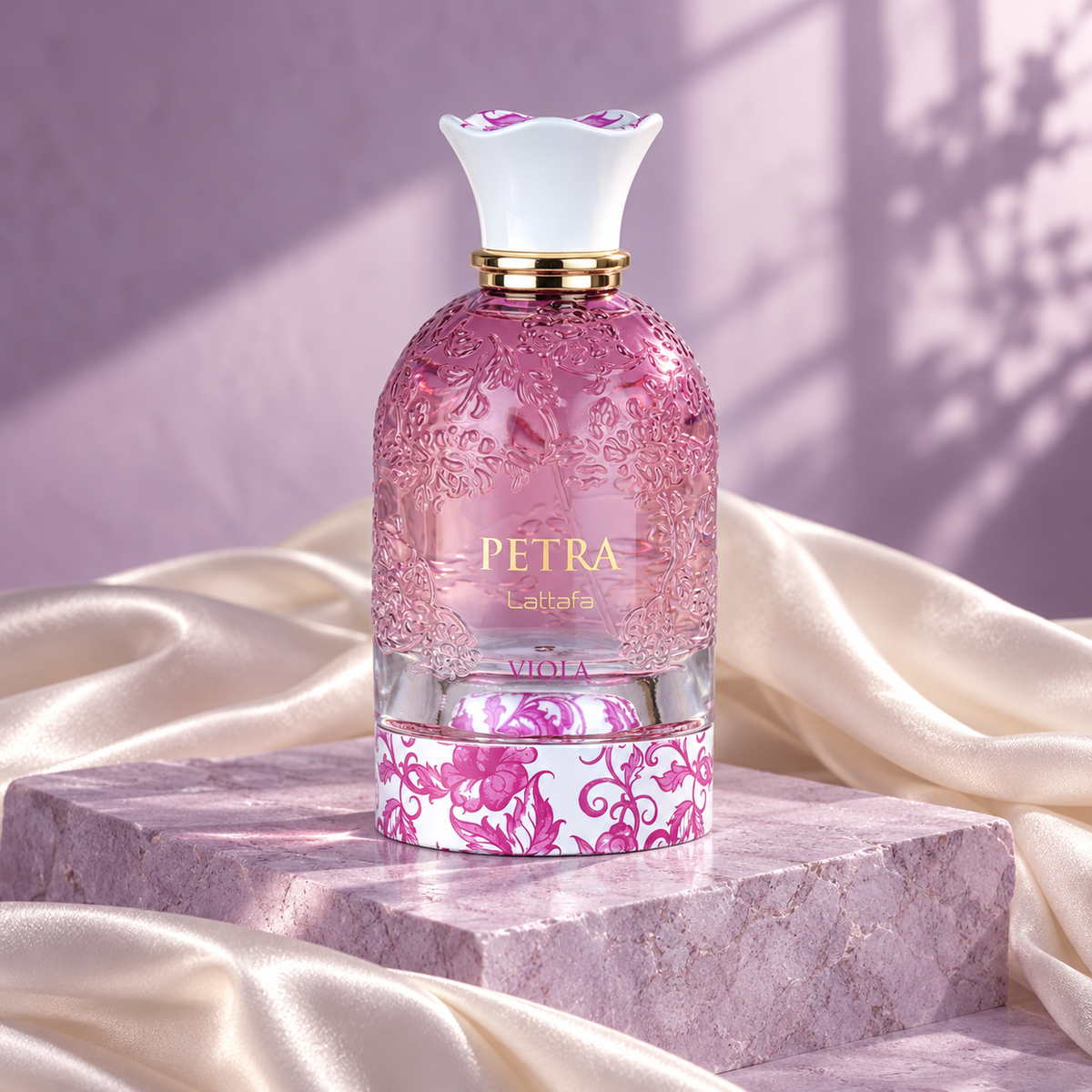 Lattafa Petra Viola pink bottle on a lilac stone plinth with ivory silk and soft window light
