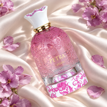 Lattafa Petra Viola embossed pink bottle lying diagonally on ivory silk with purple petals