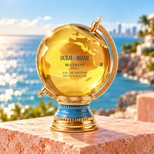 Dubai Miami perfume bottle with gold globe and blue pedestal against a coastal backdrop